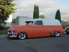 an orange and white classic car parked on the side of the road in front of a house