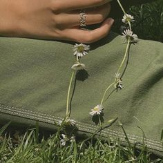 a woman's hand holding onto a flower in the grass with daisies growing out of it