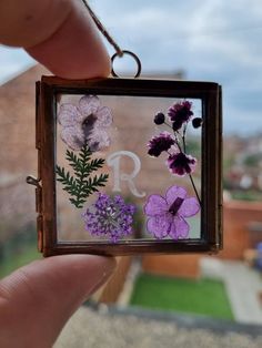 a person holding up a small glass block with flowers on it and the letter r