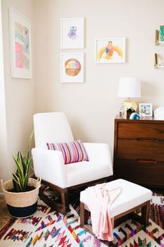 a white chair and foot stool in a room with pictures on the wall behind it