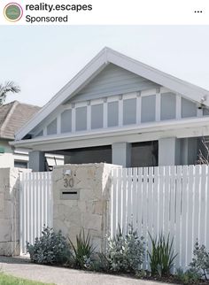 a house with a white fence in front of it and some plants on the side