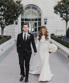 a bride and groom are walking down the street holding hands in front of a building