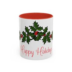 a red and white coffee mug with holly leaves on it's side, says happy holidays