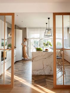 a woman standing in a kitchen next to an oven and counter top with a marble island