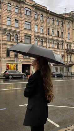 a woman holding an umbrella while standing on the side of a road in front of a large building