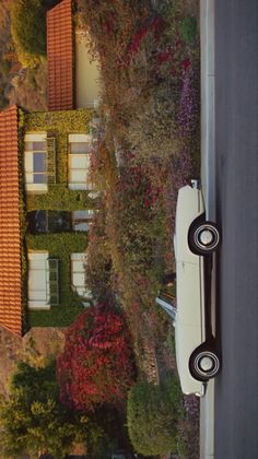 an old white car parked in front of a house on the side of a road