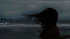 a woman standing on top of a beach next to the ocean under a cloudy sky