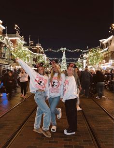 three girls are standing on the street in front of christmas lights