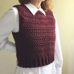 a woman wearing a crocheted sweater vest and white shirt with her hands on her hips