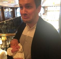 a man holding a baby in his arms while wearing a black cardigan and white striped shirt