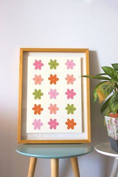 a potted plant sitting next to a framed flower print on a wall above a table