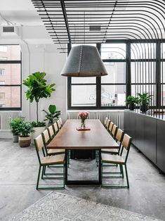 a long table with chairs around it in front of large windows and potted plants