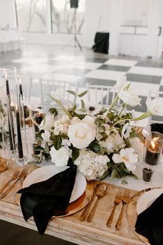 the table is set with white flowers and black napkins, gold chargers and candles