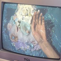 an old tv with the screen turned on and hands reaching for something out of it