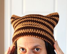 a woman wearing a knitted cat hat while holding her hair up to her ears