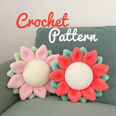 two crocheted flowers sitting on top of a gray couch next to a pillow