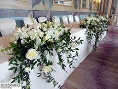 white flowers and greenery are arranged on the long table in this banquet hall setting