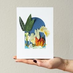 a hand holding up a card with flowers and plants