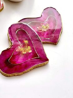 two pink heart shaped cookies sitting on top of a white table next to a cup