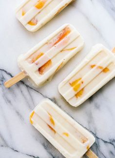 three popsicles sitting on top of a white marble counter covered in orange and yellow toppings