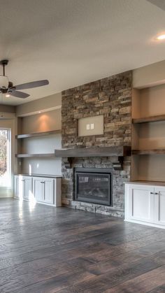 an empty living room with stone fireplace and built - in shelving