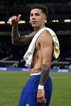 a man with tattoos on his arm and chest standing in front of a soccer field