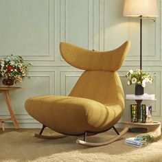 a living room with a rocking chair and books on the floor next to a lamp