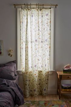 a bed sitting under a window next to a wooden table with a lamp on top of it