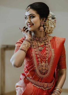 a woman in an orange and red sari with jewelry on her neck, smiling at the camera