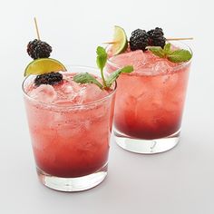 two glasses filled with ice and blackberries on top of a white table next to each other