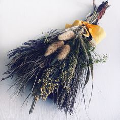 an arrangement of dried plants on a white surface with yellow ribbon tied around the stems