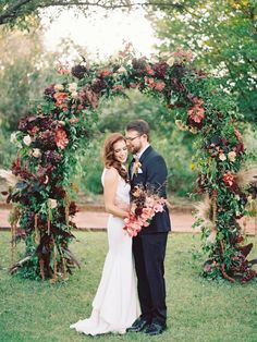 a bride and groom standing under an arch with flowers on it in the middle of their wedding day