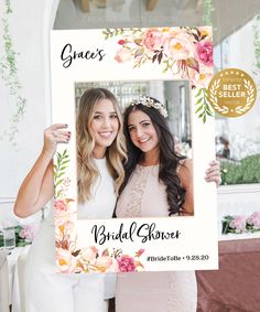 two women holding up a photo frame with flowers on it