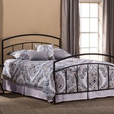 a metal bed frame with paisley print sheets and pillows on it in a bedroom setting