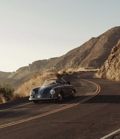 an old car driving down the road near mountains