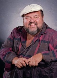 a man with a beard and a plaid shirt is posing for a photo in front of a gray background