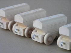 three wooden toy train cars sitting side by side on a gray surface with white wheels