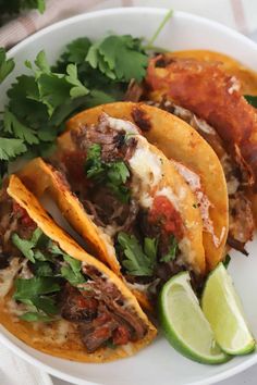 three tacos on a plate with cilantro, lime and tortillas