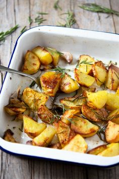 a white dish filled with potatoes and herbs