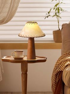 a table with a lamp on it next to a chair and potted plant in the corner