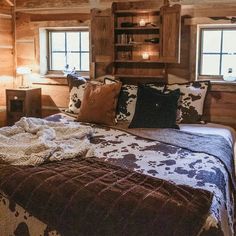 a bed in a room with wooden walls and flooring next to two windows that have lights on them