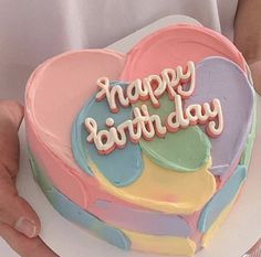 a person holding a heart shaped cake with the words happy birthday written in frosting