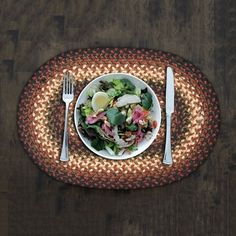 a white plate topped with salad on top of a wooden table next to a fork and knife