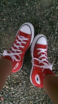 a person's feet with red converse shoes on top of rocks and gravel in front of them