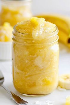 a glass jar filled with yellow liquid next to bananas and spoons on a table