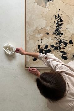 a woman is painting on the wall with black paint and white paper in front of her