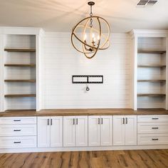 an empty room with white cabinets and wood flooring on the walls is lit by a chandelier