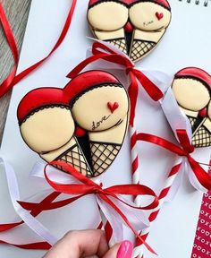 two decorated heart shaped cookies on top of a piece of paper next to red ribbon