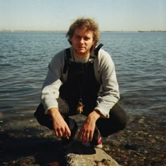 a man squatting down on a rock by the water