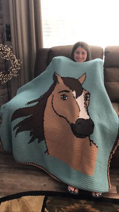 a woman sitting on a couch holding a blanket with a horse drawn on it